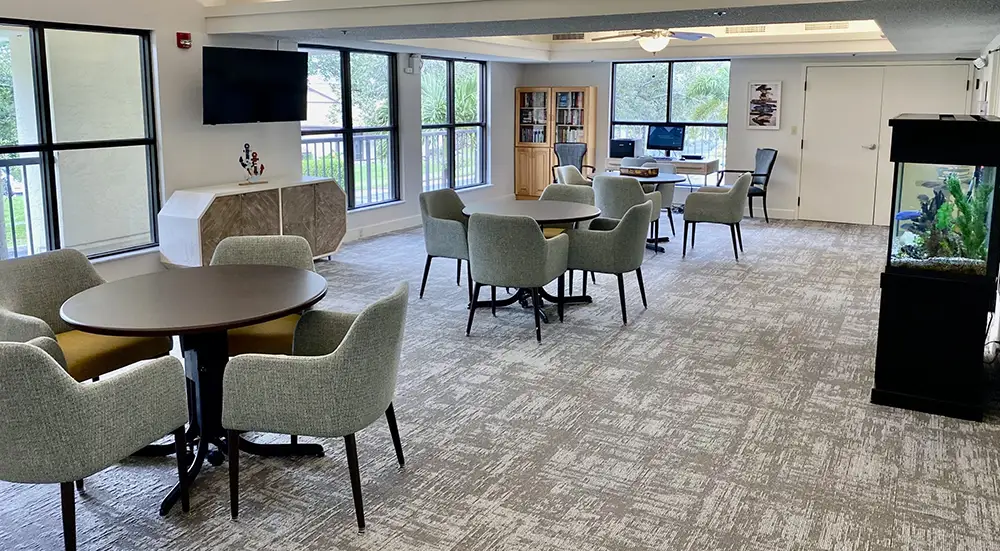 Spacious resident lounge at Springwood Court with tables, chairs, bookshelves, and a large fish tank.